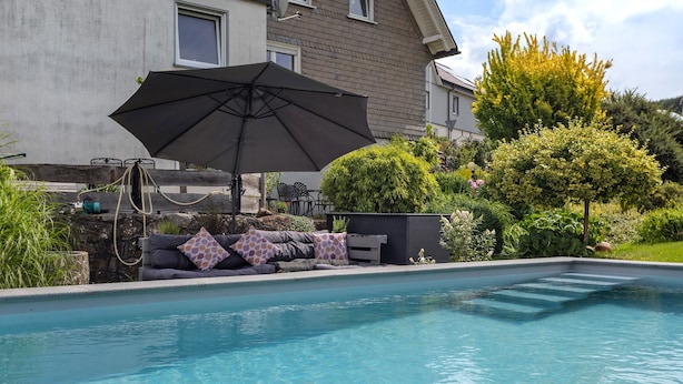 A swimming pool with a sofa and an umbrella, surrounded by greenery and a house. - Apartment 'Selbecke' with Pool and Garden (Kirchhundem)