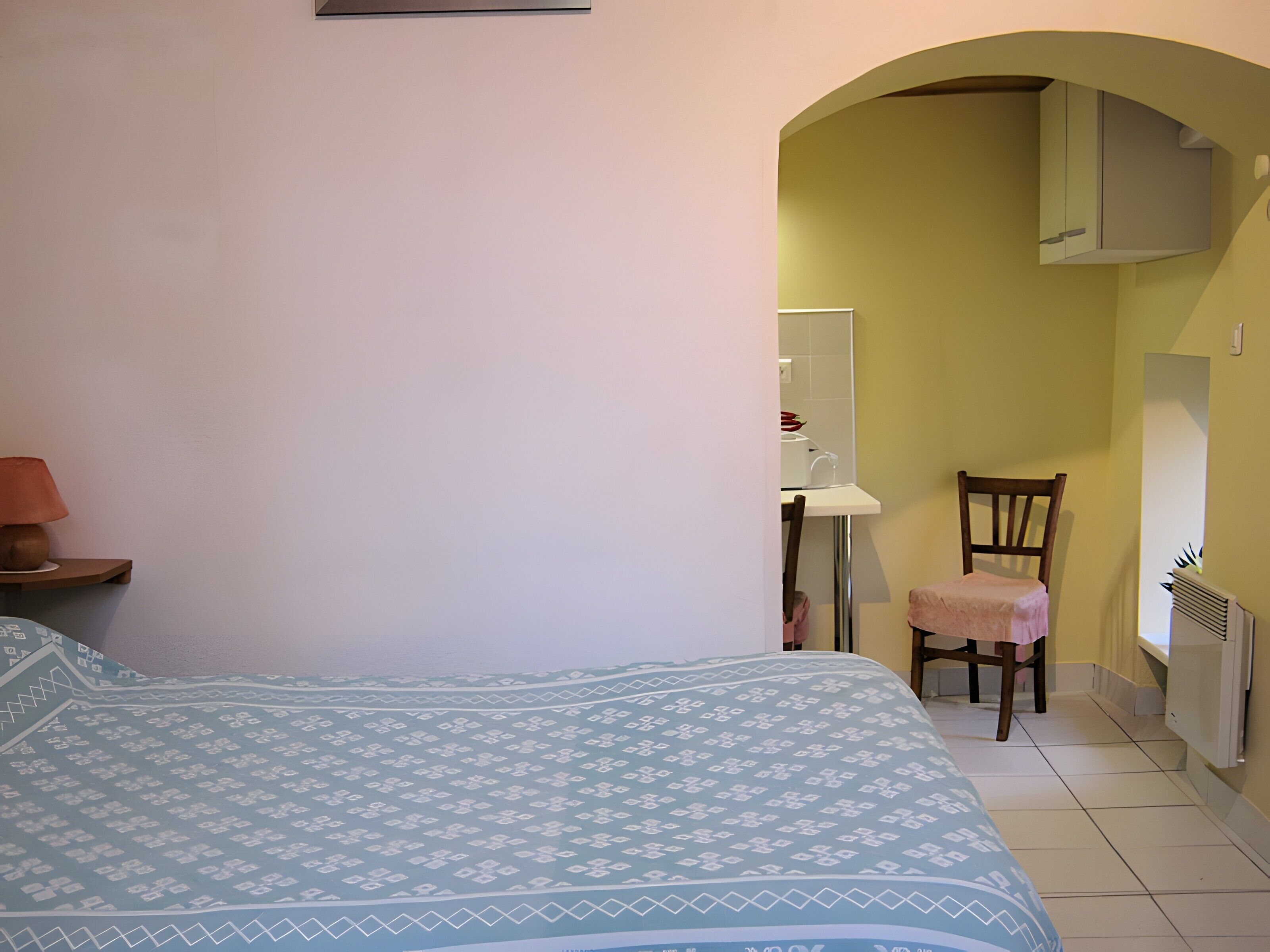 A bedroom with a bed, a chair, a desk, and a radiator.