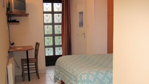 A bedroom with a bed, a desk with a chair, a television, and a window with curtains.