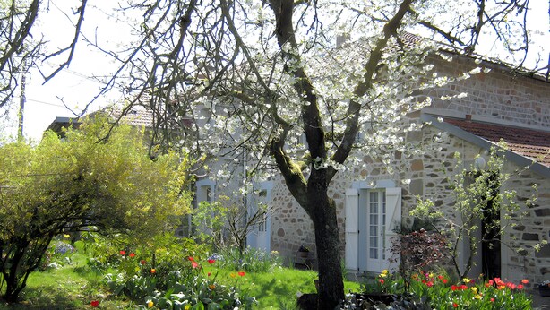 A stone building with a garden in front, surrounded by trees.