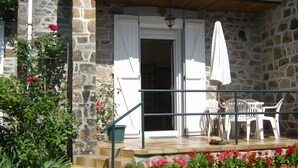A stone building with a wooden porch, white shutters, and a potted plant with red flowers.