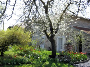 A stone building with a garden in front, surrounded by trees.