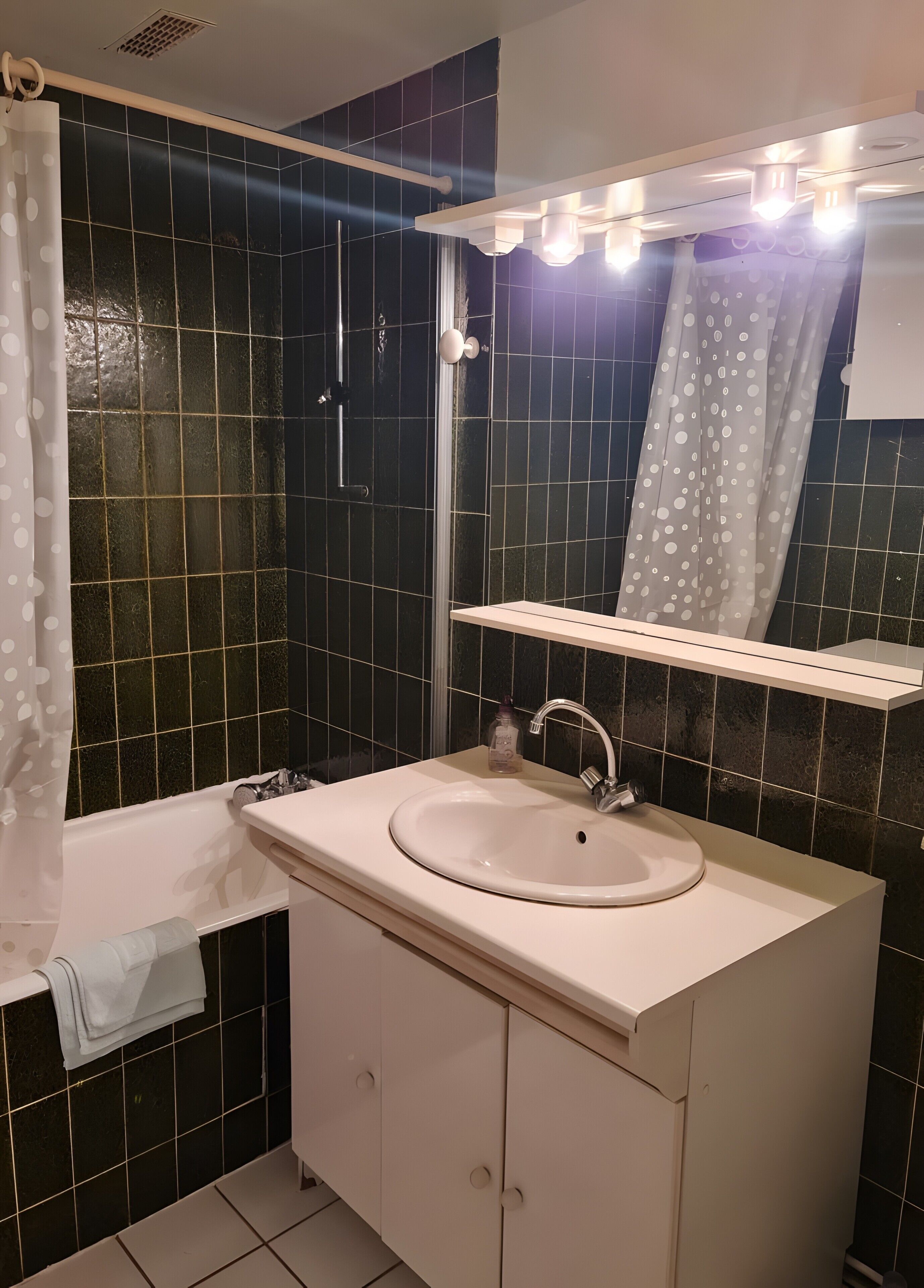 A bathroom with a white sink, mirror, and black tiled walls.