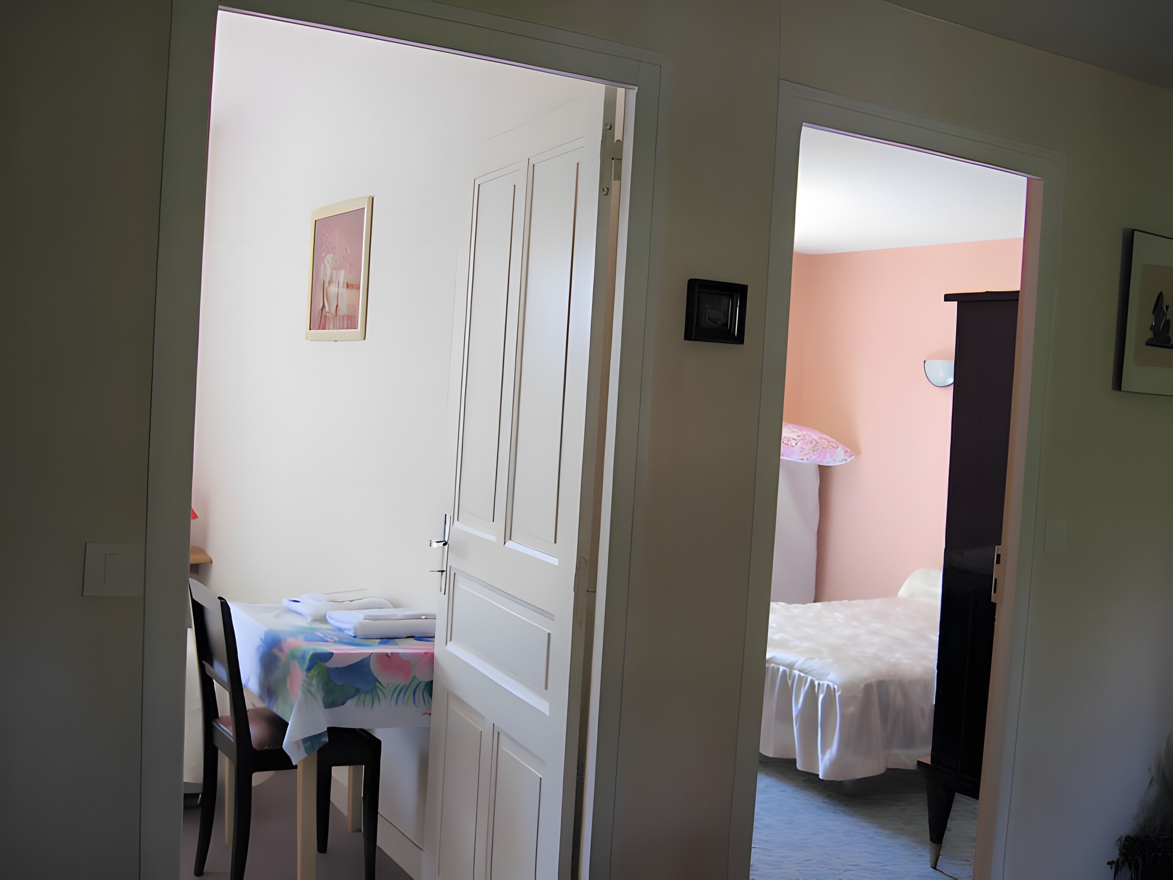 Um quarto com uma cama, uma mesa com cadeira e uma porta que dá para outro cômodo.