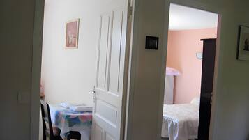 Um quarto com uma cama, uma mesa com cadeira e uma porta que dá para outro cômodo.