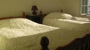 A bedroom with two beds, a nightstand with a lamp, and a window.