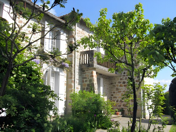 A stone building with a balcony, surrounded by greenery and trees.