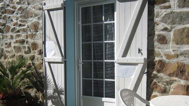 A stone wall, a white door with a window, a white chair, and a potted plant.