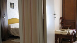 A bedroom with a bed, a wooden wardrobe, a chair, and a table with towels.