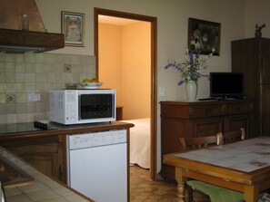 Kompakti keittiö, jossa on mikroaaltouuni, astianpesukone, ruokapöytä tuoleineen, televisio ja maljakko, jossa on kukkia.