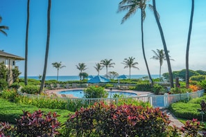 Uma área de piscina em resort, com palmeiras, vista para o oceano e um cercado branco.