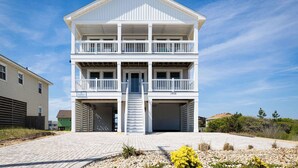 A two-story building with a balcony on the second floor, a garage on the ground floor, and a paved driveway. - Spacious KDH Getaway with Pool, Near Beach (Kill Devil Hills)
