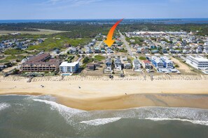 Vue aérienne d’un quartier résidentiel situé sur la côte, avec des maisons, une plage et un grand bâtiment doté d’un toit en forme de flèche.