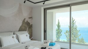 A modern bedroom with a large bed, a view of the sea, and a painting on the wall.