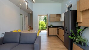 A modern kitchen with wooden cabinets, a black refrigerator, and a dining area with a grey sofa and yellow cushions.