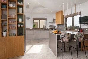 A modern kitchen with a central island, bar stools, and a variety of decorative items on shelves. - Villa Olive Grove Zadarvillas (Zemunik Donji)