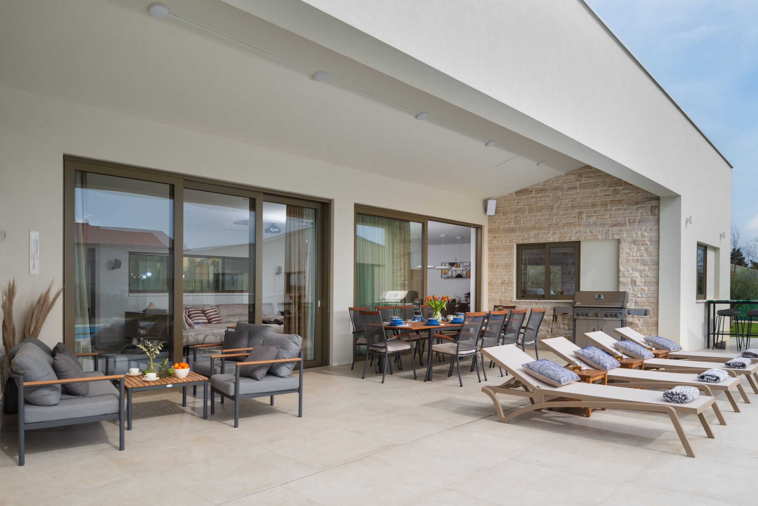 A modern outdoor living area with a dining table, chairs, lounge chairs, and a barbecue grill.