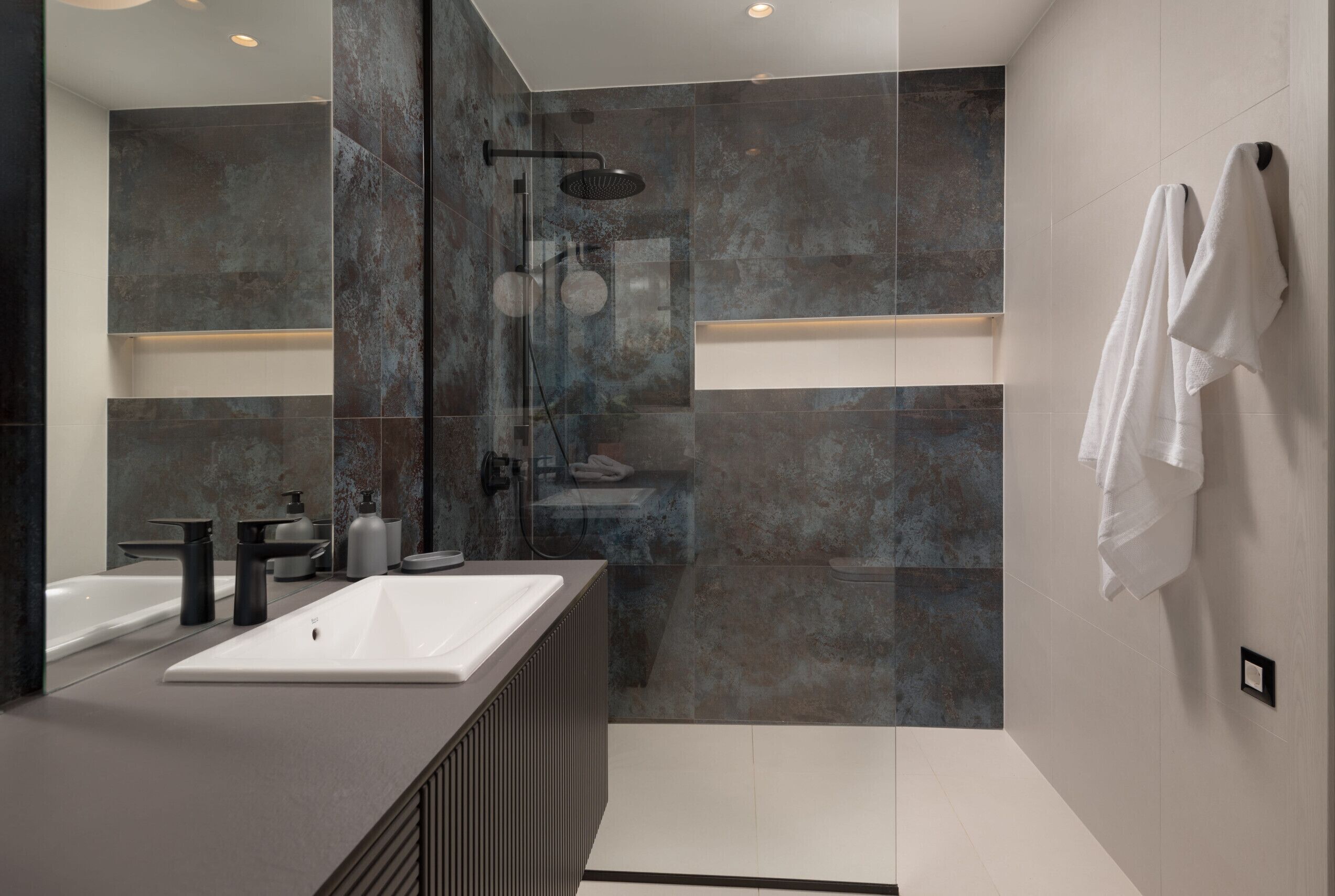 Un baño moderno con un espejo grande, dos lavamanos, una ducha y un perchero para toallas.