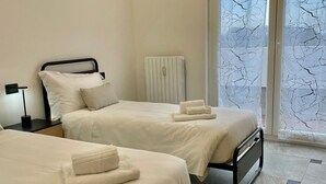 Zwei Betten mit weißen Leinen und Handtüchern, ein Nachttisch mit Lampe und eine Heizung.