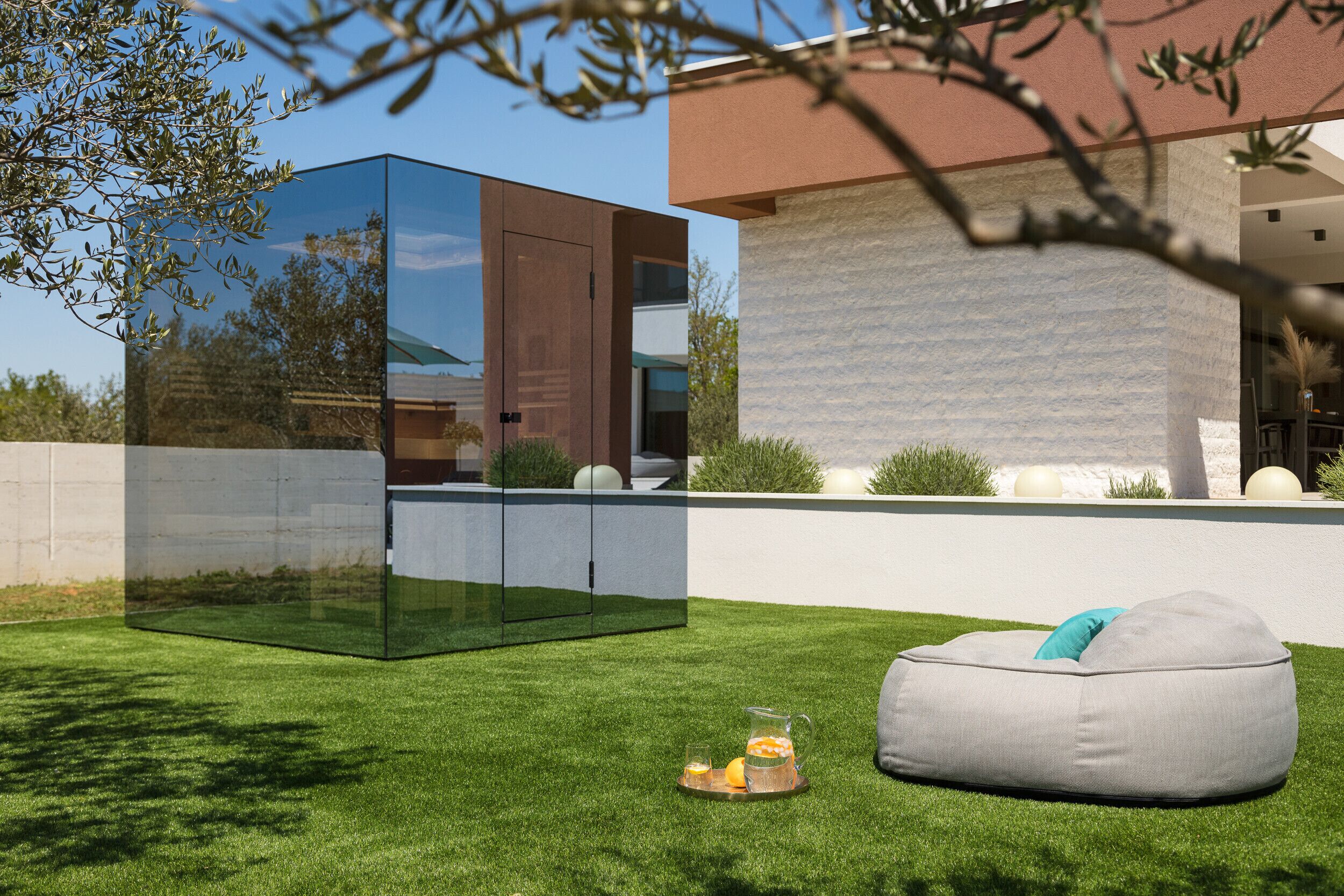 Ein moderner Außenbereich mit Glasbau, einem grauen Sitzsack und einem kleinen Tisch mit einem Getränk.