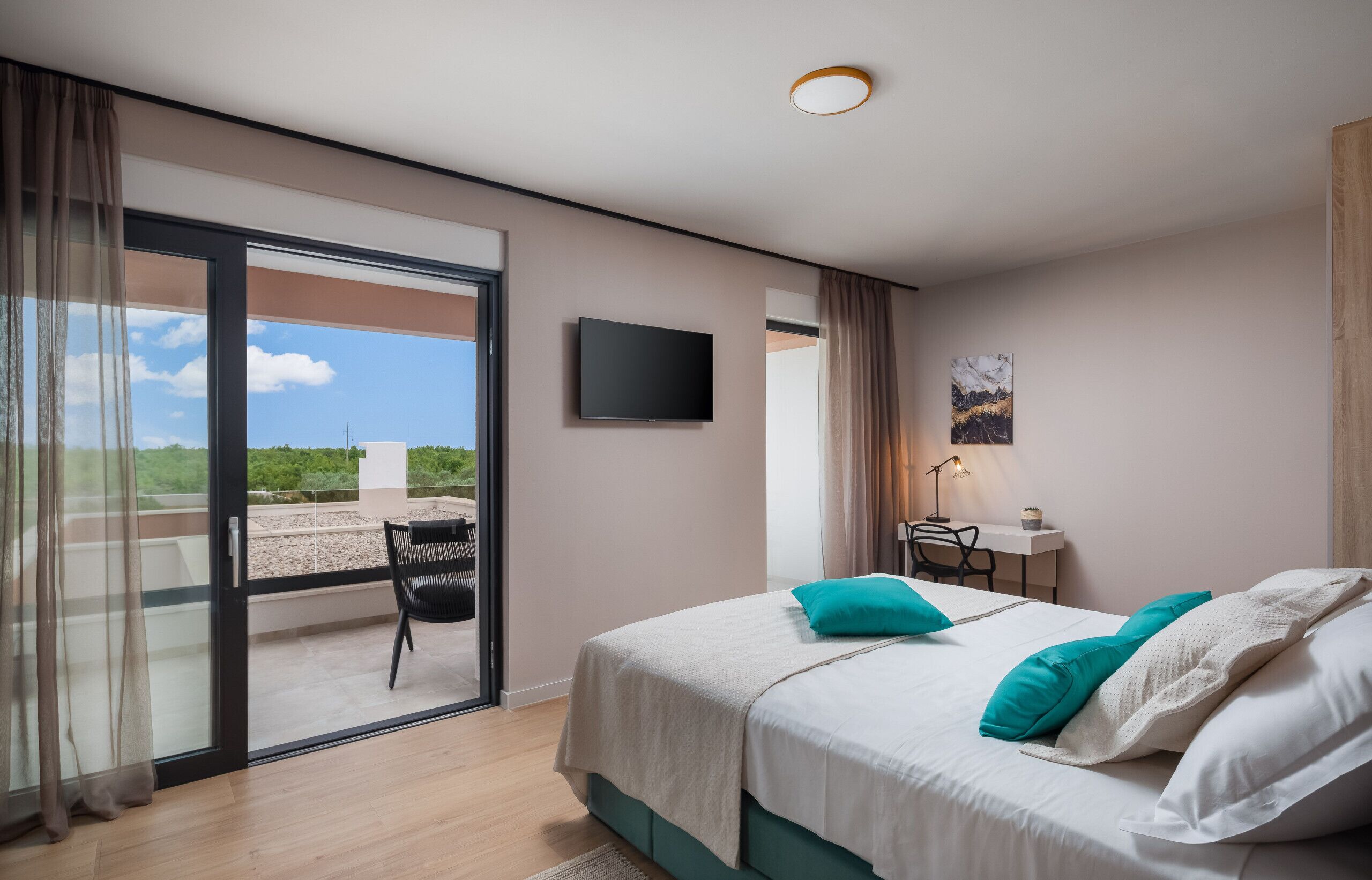 Un dormitorio con cama, escritorio, silla, televisor y balcón con una silla.