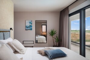 Una habitación de hotel moderna con una cama grande, una mesita de noche, un espejo, un ventanal con vistas y un cuadro en la pared.