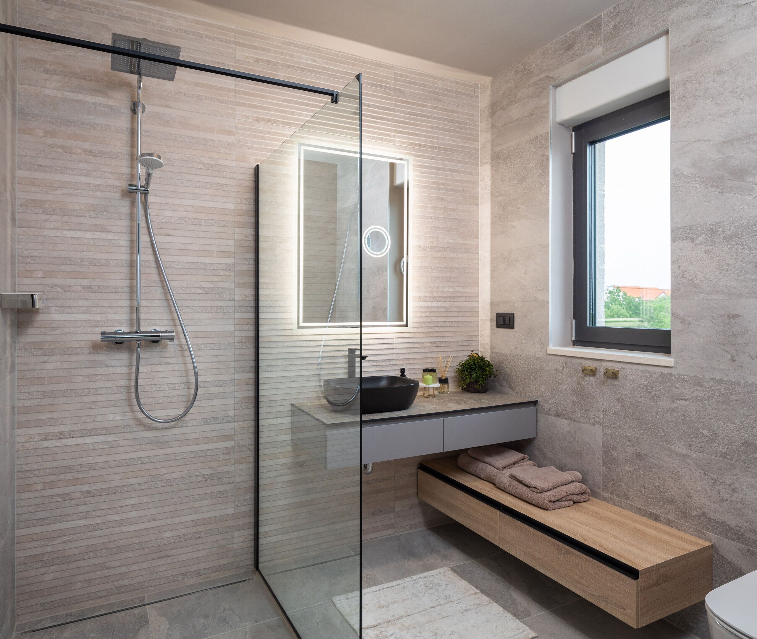 A modern bathroom with a glass-enclosed shower, a built-in sink with a mirror, and a window providing natural light.
