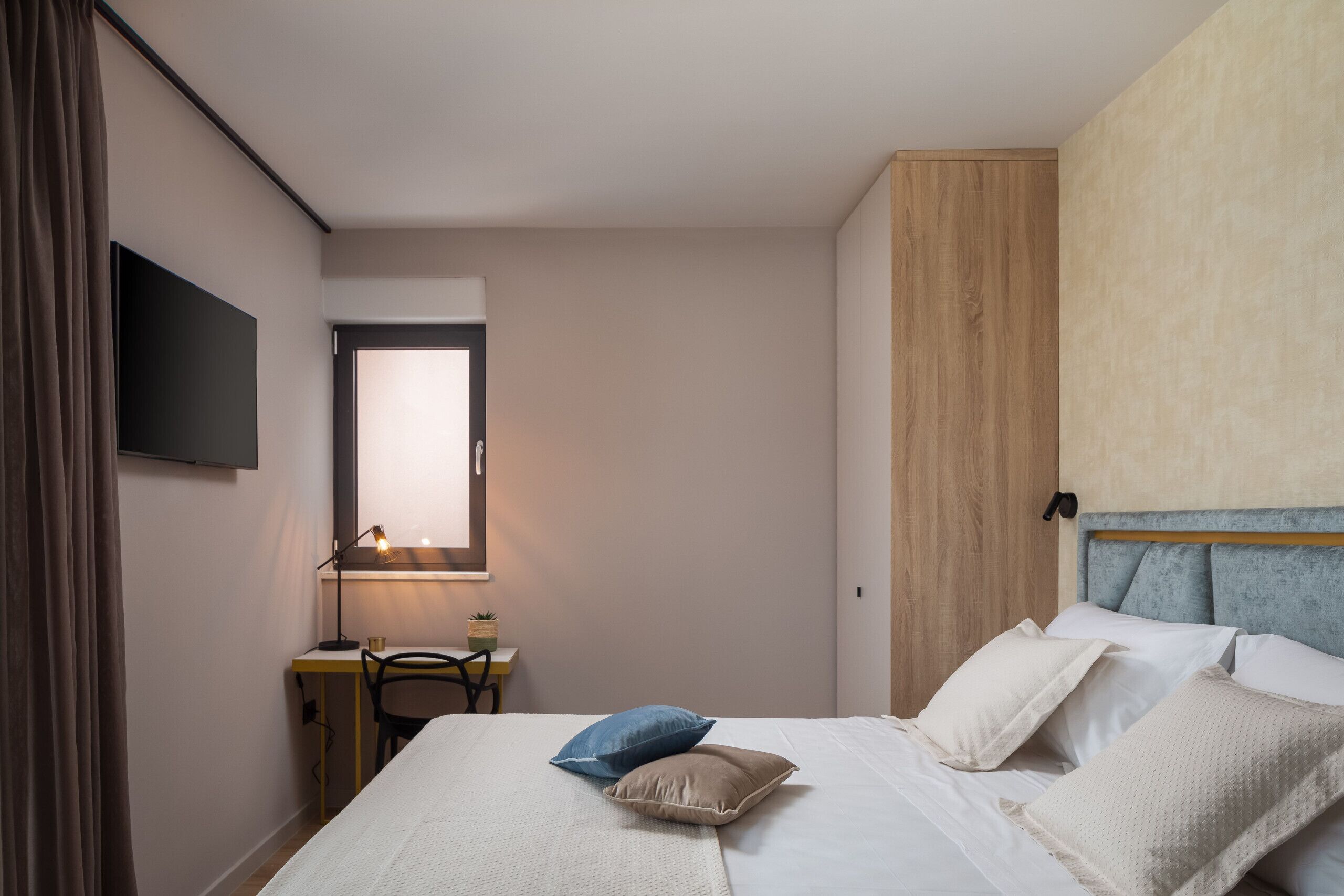 Un dormitorio con cama, escritorio, silla, televisor y ventana.