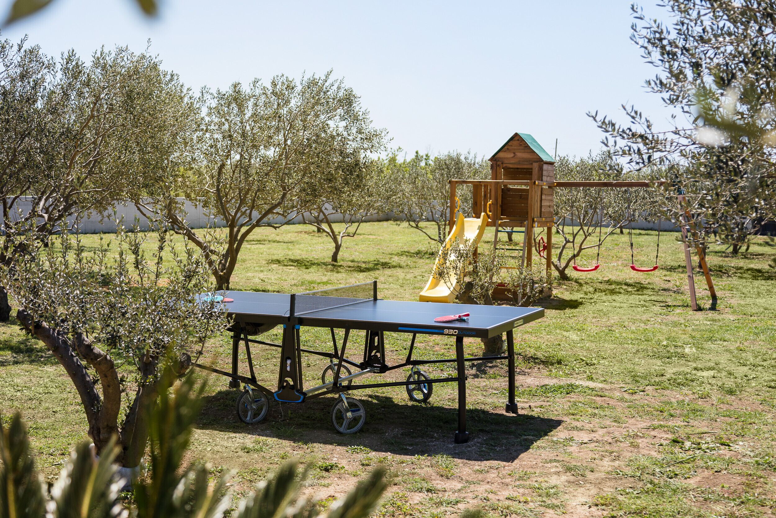 A ping pong table in a grassy outdoor area with a playground in the background.
