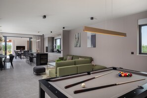 Una sala de estar moderna con mesa de billar, sofá verde y comedor con sillas y mesa.