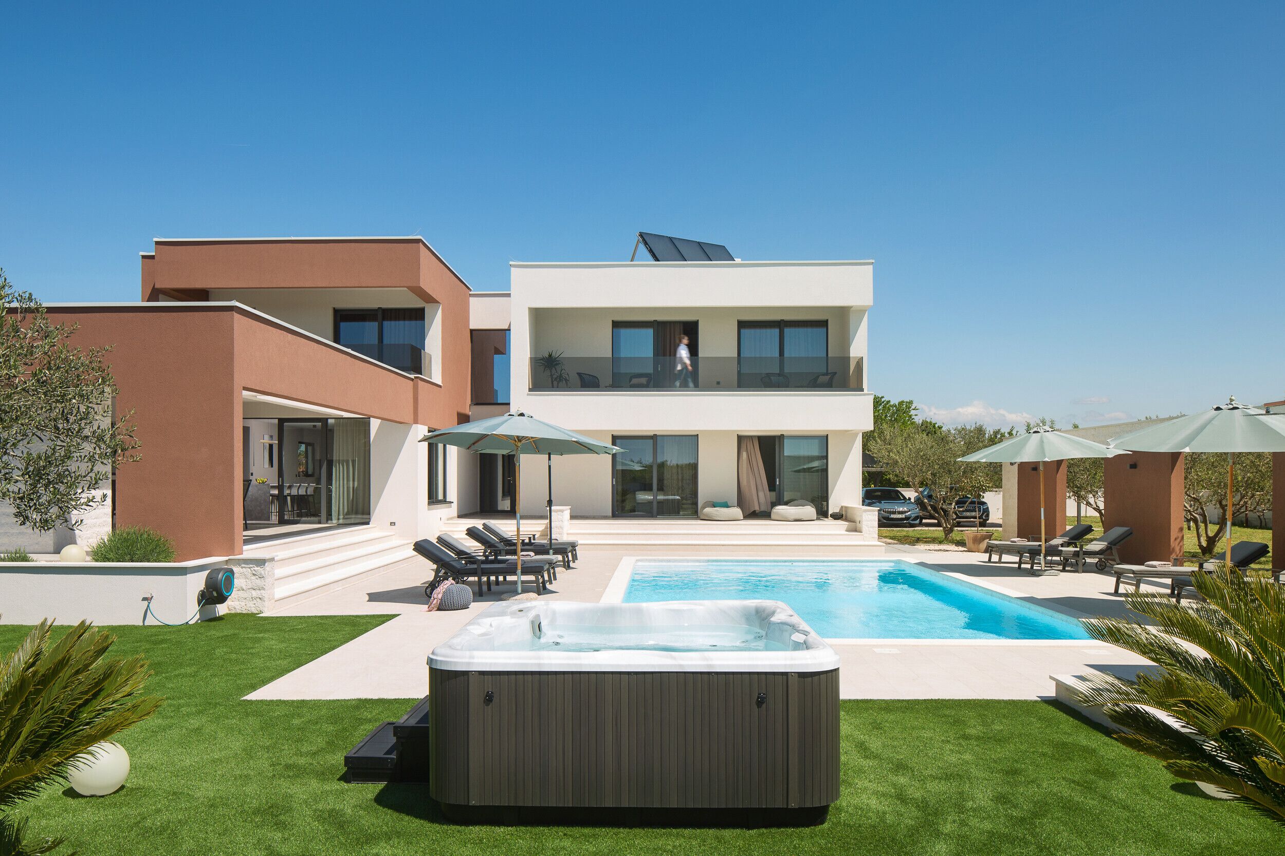 A modern two-story house with a swimming pool, a hot tub, and outdoor seating.