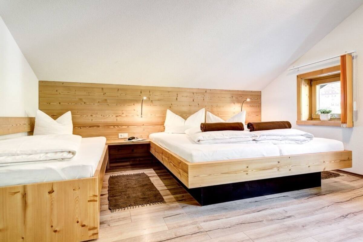 A bedroom with a sloped ceiling, wooden headboard, two beds, a nightstand, a bedside table, a window with a view, and a rug.