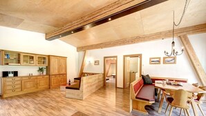 A spacious room with wooden flooring, a dining area with a bench, and a kitchen with wooden cabinets. - Bocks Apartments 61 (Dalaas)