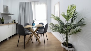 A modern kitchen with white cabinets, a dining area with a wooden table and chairs, and a large potted plant. - Imprenta Sorolla by Concept (València)