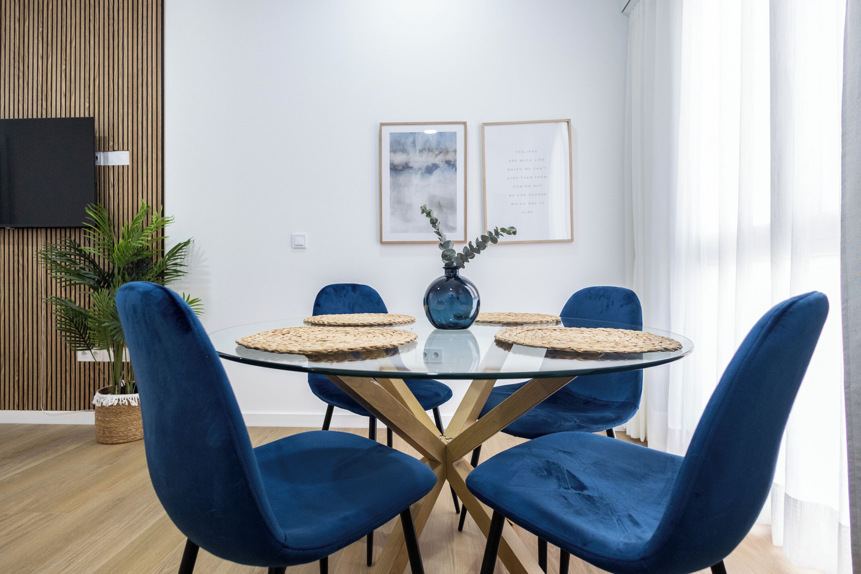 Un moderno comedor con una mesa de vidrio, sillas azules y un jarrón con plantas.