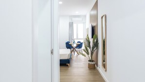 A corridor with a bed, a desk, and chairs, leading to a room with a window. - Imprenta Sorolla by Concept (València)