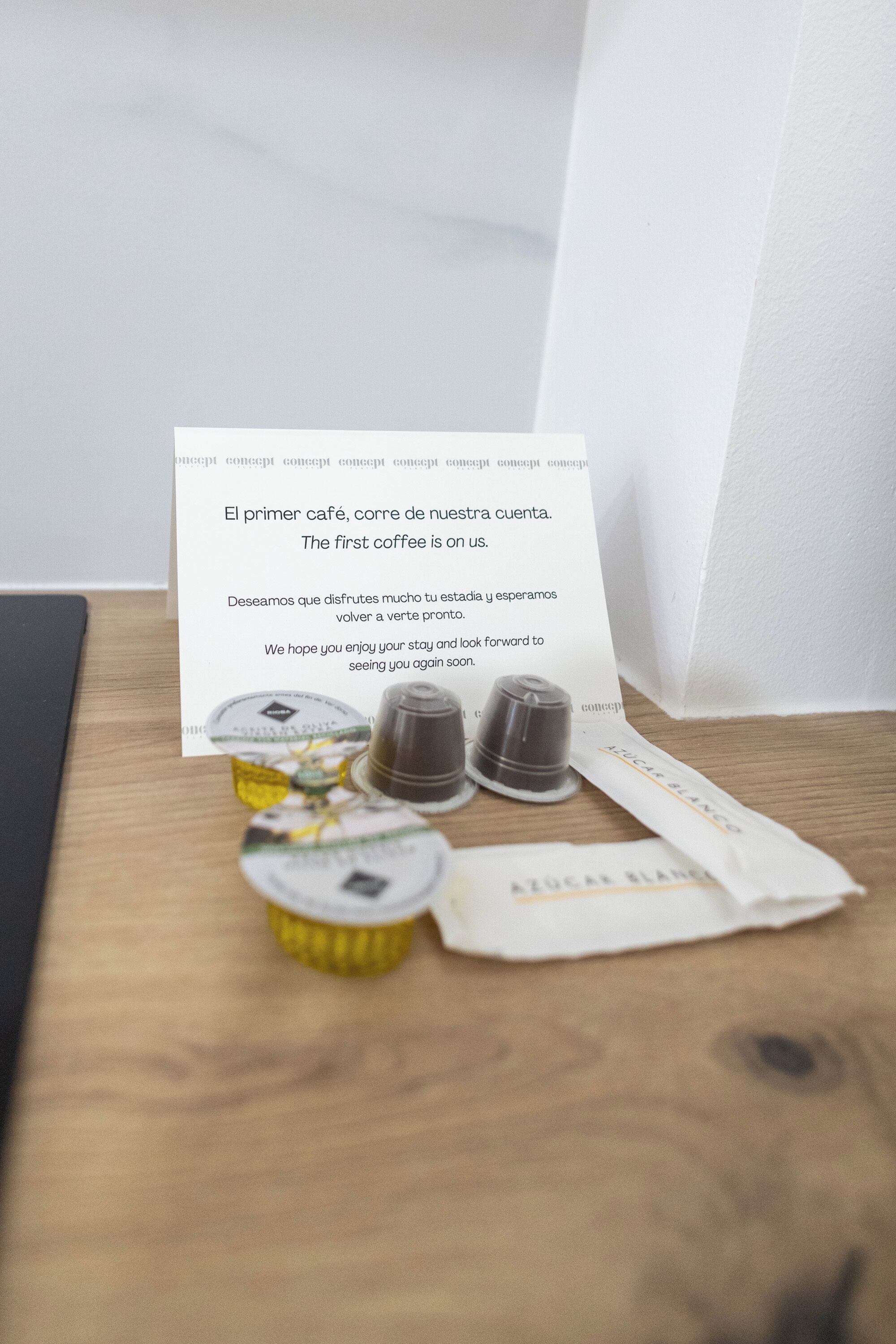 Una mesa de madera con una taza de café, un paquete de café y una tarjeta con texto en español.