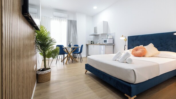 A modern hotel room with a bed, a small kitchenette, a dining area, and a potted plant. - Imprenta Sorolla by Concept (València)