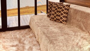Una habitación acogedora con un ventanal grande con vistas a un lago, techo de madera y un sofá mullido con cojines estampados.