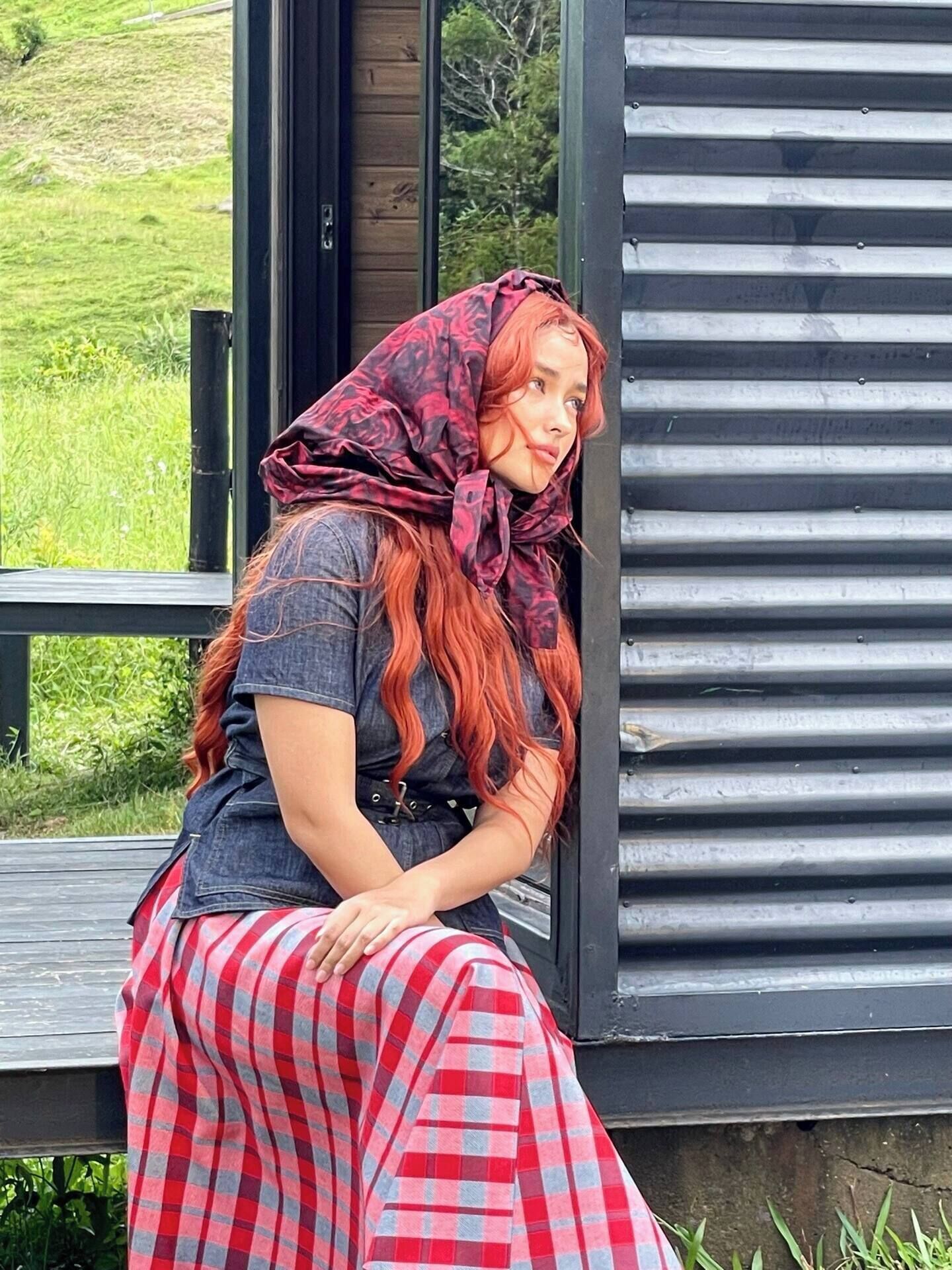 A person sitting on a wooden bench outside a building with large windows.