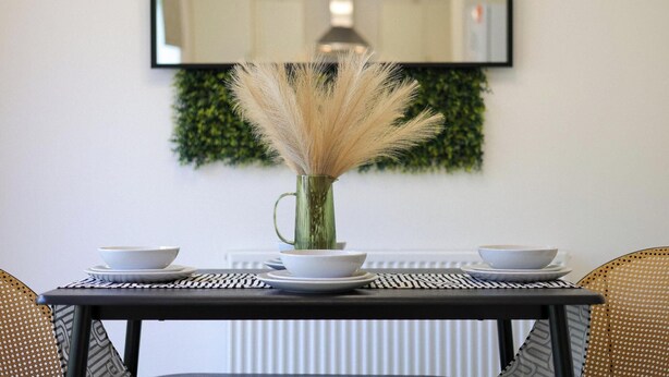 A dining table with white plates and bowls, a vase with pampas grass, and a mirror above a green wall. - Modern 4BR House in the Centre Spacious & Ideal for Families and Contractors (Overdale)
