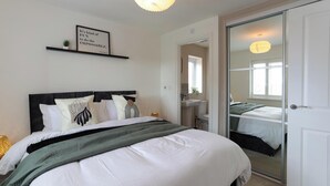 A bedroom with a bed, a bedside table, a mirror, a window, and a door. - Modern 4BR House in the Centre Spacious & Ideal for Families and Contractors (Overdale)