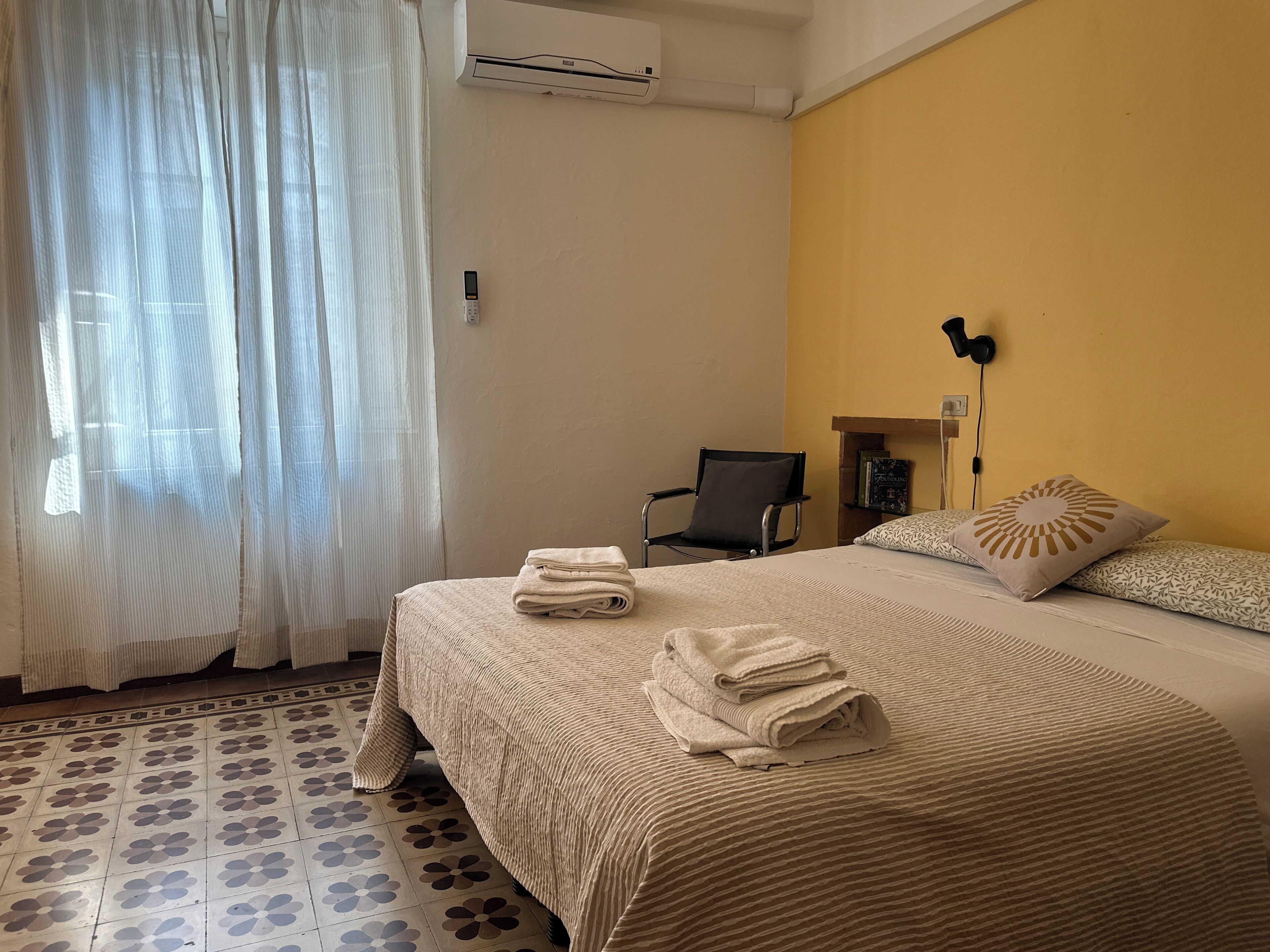 Habitación de hotel con una cama, una silla, un escritorio y un equipo de aire acondicionado.