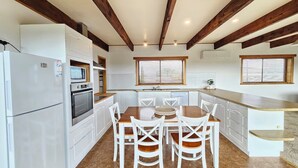 A kitchen with white cabinets, a wooden dining table, and chairs. There is a refrigerator, an oven, and a sink.
