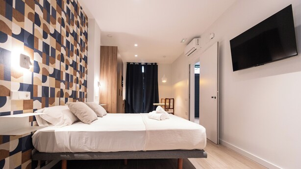 Quarto de hotel moderno com uma cama grande, televisão de tela plana na parede e um design de parede estampado.