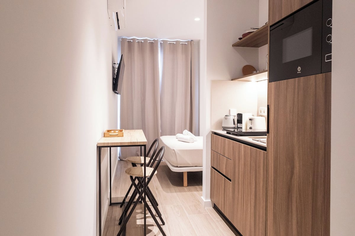 A compact kitchen with a dining area, wooden cabinets, and a flat-screen TV mounted on the wall.