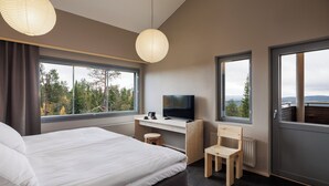 Une chambre d’hôtel moderne dotée d’un grand lit, d’un bureau avec une télévision et offrant une vue sur les arbres par les fenêtres.