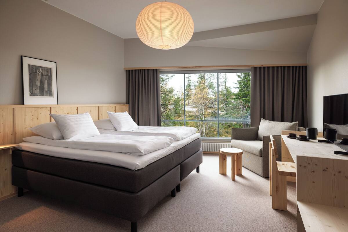 Une chambre d’hôtel moderne dotée d’un grand lit, d’un canapé, d’un bureau et offrant une vue sur les arbres par la fenêtre.