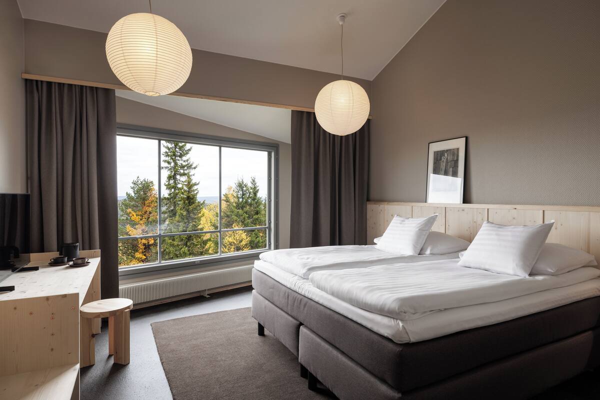 Une chambre moderne avec un grand lit, un bureau et une vue sur les arbres par la fenêtre.