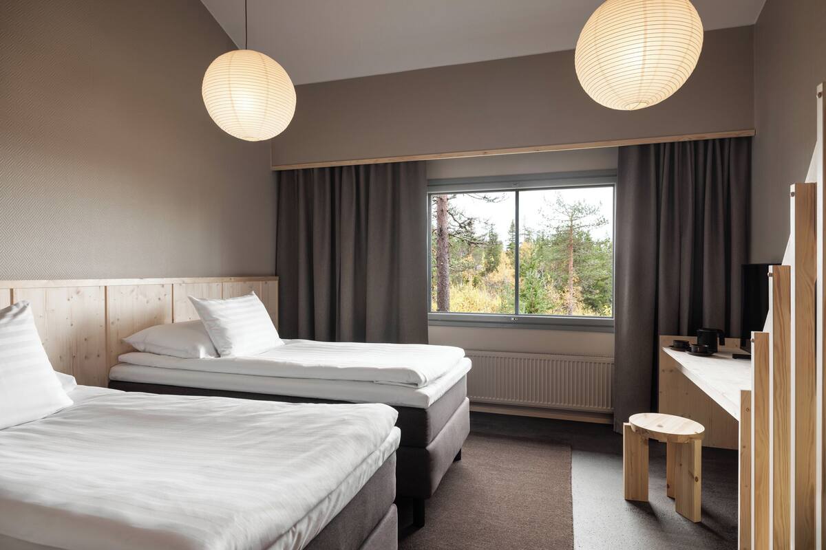 Une chambre d’hôtel moderne équipée de deux lits, d’un bureau, d’une chaise et d’une grande fenêtre avec des rideaux.